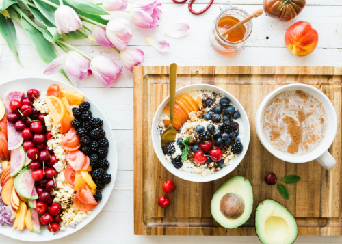 A variety of healthy foods including leafy greens, fruits, whole grains, nuts, fish, and plant-based proteins arranged on a kitchen table.